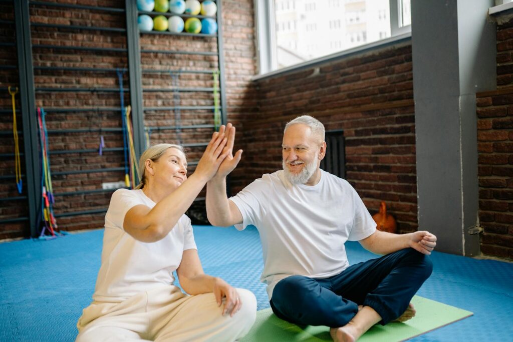 Energetic senior couple enjoying yoga, sharing a joyful high-five at the gym.