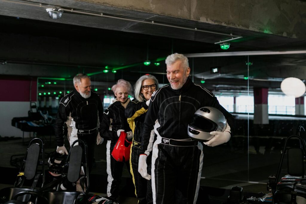 Group of senior adults having fun go-kart racing indoors with safety gear.
